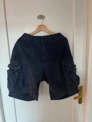 Blue Polo Ralph Lauren Cargo Shorts - Baggy shorts köpta i London, använt ett fåtal gånger. Har ett par fläckar och märken. ‼️Det står storlek 38 men på mig som har cirka 42 är de lösa i midjan‼️