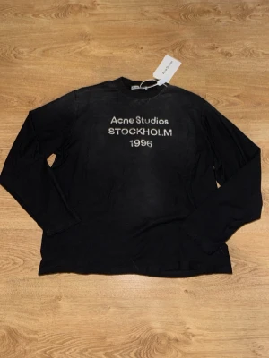 Acne Studios longsleeve - Svart långärmad tröja från Acne Studios med tryck 'Acne Studios STOCKHOLM 1996' på bröstet. Tröjan har rund hals och en avslappnad passform. Perfekt för en stilren och enkel look. Helt ny aldrig använd storlek M