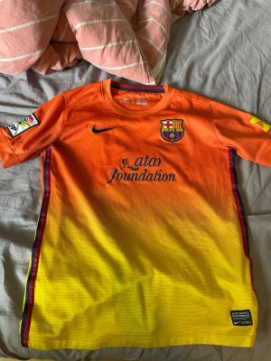 Barcelona Xavi matchtröja orange/gul - Snygg FC Barcelona matchtröja från Nike i orange och gul färg med Xavi och nummer 6 på ryggen. Tröjan har klubbmärke, Nike-logga och Qatar Foundation-tryck på framsidan samt UNICEF-tryck bak. Korta ärmar och autentiska detaljer. Perfekt för fotbollsfans!