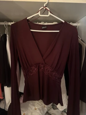 Vinröd topp från Gina Tricot - Snygg vinröd topp från Gina Tricot med lång ärm och v-ringning. Toppen har spetsdetaljer under bysten som ger en extra touch. Perfekt att styla med jeans eller kjol för en trendig look.