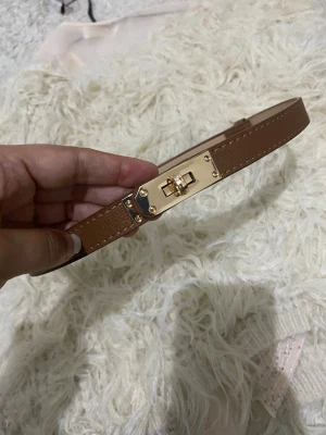 Beige smalt bälte med gulddetalj - Snyggt och stilrent smalt bälte i brun med en liten guldfärgad detalj på spännet. Perfekt för att lyfta en outfit och passar till både jeans och klänning. Enkel design som känns modern och trendig.