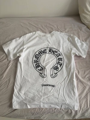 Vit Chrome Hearts t-shirt - Säljer en vit t-shirt från Chrome Hearts med stort svart tryck på ryggen och mindre logga på bröstet. Klassisk passform och rund hals. Perfekt för dig som gillar streetwear och vill sticka ut med en ikonisk design. Pris kan diskuteras, har tags till men inte på tröjan