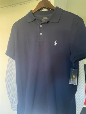  Polo Ralph Lauren pike marinblå M - Säljer denna fina helt nya Ralph lauren piken, färg: marinblå och storlek M                         Modellen är custom slim fit och har knappar framtill.  Orginalpris: 1695 kr från Zalando 