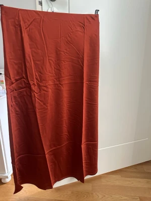 Rostbrun långkjol i satin - Snygg rostbrun långkjol i ett glansigt satinliknande material. Kjolen har en rak och enkel design utan synliga detaljer eller mönster, vilket ger ett stilrent intryck. Perfekt för dig som gillar minimalistisk och trendig stil.