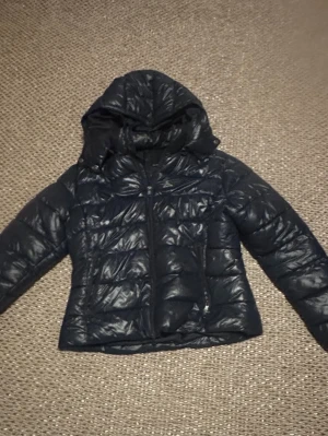 Lager 157 pufferjacka  - Säljer en mörkblå pufferjacka med luva och dragkedja framtill. Jackan har en quiltad design och är vadderad för extra värme. Perfekt för kalla dagar och har en klassisk, enkel look som passar till det mesta. Storlek L men passar M eller S. Skriv till mig om frågor!