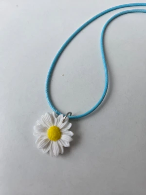 Halsband med prästkrage och blått snöre - Sött halsband med en vit prästkrage som har gul mitt, hängande på ett tunt blått snöre. Halsbandet har justerbart metallspänne och passar fint till sommaren. Gjort för hand av mig i polymerlera. 