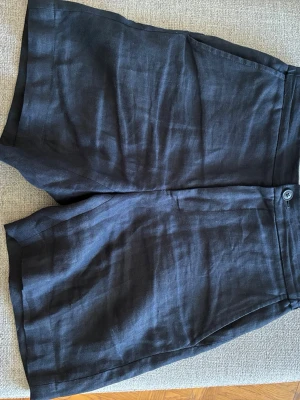 Marinblåa linne shorts - Snygga och stilliga marinblåa shorts i linne från These Glory Days köpta på Volt. Klassisk design med knapp och dragkedja framtill samt fickor i sidorna. Perfekta för varma dagar och enkel att matcha med olika toppar. Storlek 44.