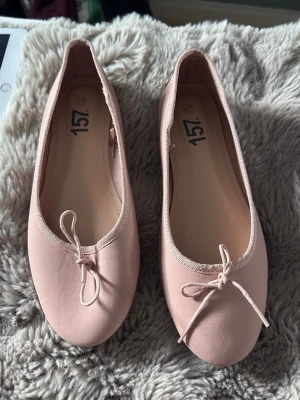 Ljusa rosa ballerinaskor med rosett - Säljer ett par ljusrosa ballerinaskor från 157. Skorna har en klassisk rund tå, dekorativ rosett framtill och är gjorda i ett mjukt, matt material. Perfekta för dig som gillar en enkel och söt stil.