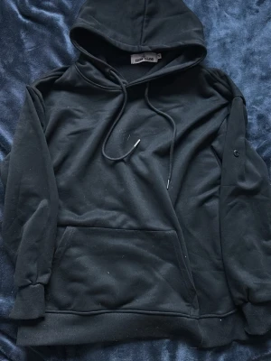 Svart hoodie från Stone Island - Säljer en svart hoodie från Stone Island med klassisk huva och dragsnören. Hoodien har en stor magficka framtill och ribbade muddar vid ärmar och nederkant. Tillverkad i mjukt bomullsmaterial, perfekt för en chill och stilren look.