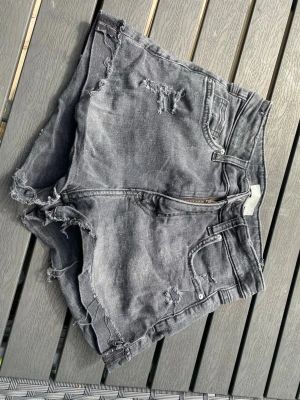 Grå slitna jeansshorts med fransar - Säljer ett par grå stretch jeansshorts med slitna detaljer och uppvikt kant. 