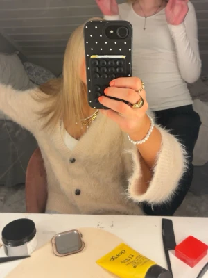 Beige fluffig kofta med knappar - Mysig beige kofta med fluffig textur och stora svarta knappar framtill. Koftan har v-ringning och långa ärmar, perfekt för lager på lager och en avslappnad men trendig look. Passar till både klänning och jeans.