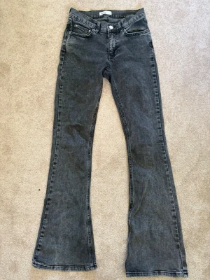 Grå bootcut jeans från Gina Tricot - Säljer ett par grå bootcut jeans från Gina Tricot med klassiska fickor och normalhög midja. Jeansen har en snygg tvättad look och är tillverkade i mjukt denimtyg med lite stretch för skön passform. Perfekta för dig som gillar retrovibbar och vill ha ett par trendiga jeans.
