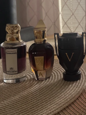Parfymer Bytes - : Penhaligon's Portraits med gulddetaljer och lejonhuvud, Xerjoff XJ med elegant guldlock och mörk bärnstensfärgad flaska samt Paco Rabanne Invictus Victory i svart troféformad flaska med gulddetaljer. Perfekta för dig som gillar unika dofter.