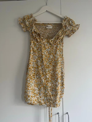 Gul blommig kortklänning från - Söt kortklänning  i vitt och gult med blommigt mönster. Tight passform