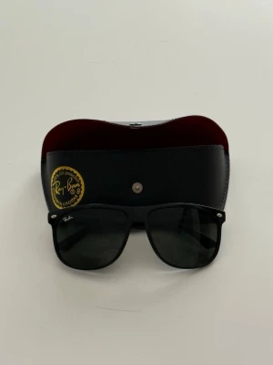 Svarta Ray-Ban solglasögon med fodral - Klassiska svarta Ray-Ban Wayfarer solglasögon med mörka glas och ikonisk form. Kommer med svart fodral med röd insida och Ray-Ban-logga. Perfekta för att lyfta din stil med en tidlös accessoar. Det finns en spricka! Se sista bilden