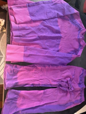 Lila underställ från Craft, storlek L - Säljer ett ribbat underställ från Craft i en cool lila färg. Setet består av långärmad tröja och långkalsonger i caprimodell, perfekt för träning eller utomhusaktiviteter. Väldigt lite använt. Materialet är mjukt och stretchigt, vilket ger bra komfort och rörelsefrihet.