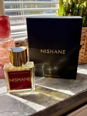 Nishane Hundred Silent Ways parfym - Nishane Hundred Silent Ways är en exklusiv parfym med elegant fyrkantig glasflaska och guldfärgad metallkork. Flaskan har en röd etikett med guldtext och kommer med en stilren svart kartong med guldfärgad logotyp. Perfekt för dig som vill ha något lyxigt och unikt. 50ml, ny 