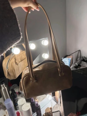 Väska  - FRÅN NA-KD HELT NY, NYPRIS 499S.  En stilren brun/khaki väska. Väskan har ett stort huvudfack med dragkedja och en praktisk ytterficka på baksidan. Materialet är slätt och ger ett klassiskt intryck, perfekt för dig som gillar minimalistisk design. 