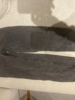 Grå raka jeans med vintagekänsla - Säljer ett par grå jeans med rak passform och klassisk femficksdesign. Jeansen har en tvättad vintage-look och är tillverkade i denim. Perfekta för en avslappnad och trendig stil.