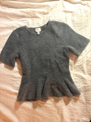 Grå ribbad topp med volang - Superfin grå stickad tröja med volang. Endast använd en gång, väldigt bra skick! Hör av er vid frågor om pris eller annat!💗
