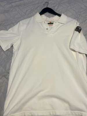 Vit pikétröja från Parajumpers - Klassisk vit pikétröja från Parajumpers med krage, knappar vid halsen och ett snyggt patch på ärmen. Tillverkad i mjuk bomull som känns skön mot huden. Perfekt till jeans eller shorts för en clean och enkel stil.