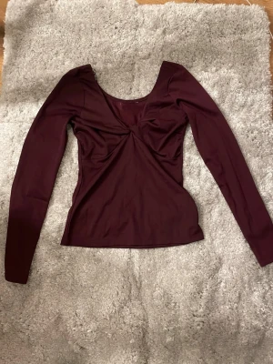 Vinröd långärmad glittrig topp med twist  - Snygg vinröd topp med lång ärm och twistad detalj framtill som är lite glittrig med djup urringning. Jätte fin och har bara använt en gång men lapparna är bort klippta för att jag störde mig på dom under den kvällen jag hade den på mig. 38 cm frön armhålan och ner, från axel till axel är den 36 cm skriv gärna om du vill ha mer information 🫶🏻 
