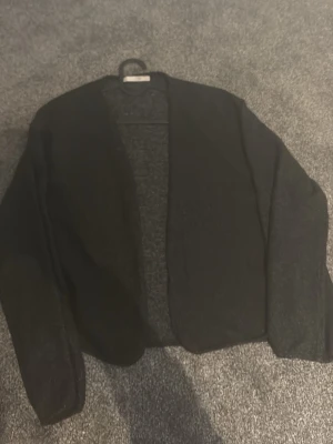 Svart öppen kofta XS - Säljer en svart öppen kofta från 157 i storlek XS. Koftan har lång ärm och är tillverkad i ett mjukt, tunt stickat material. Enkel och stilren design utan knappar eller dragkedja, perfekt att slänga över en topp.