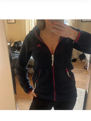 Mörkblå fleecehoodie med dragkedja - Mysig mörkblå fleecehoodie med huva och hel dragkedja framtill. Två fickor med dragkedja och rosa detaljer vid fickor och dragkedja. Perfekt för att både ha under jacka och bara som fleece vid en vårdag!  Obs: Storlek 150