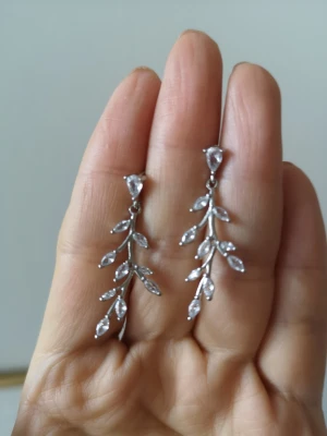 Silvriga örhängen med bladformade stenar - Säljer ett par eleganta silvriga örhängen med hängande design. Örhängena har flera små, klara stenar i bladform som ger ett glittrande och stilrent intryck. Perfekta för dig som gillar smycken med naturinspirerade detaljer och vill ha något som sticker ut.