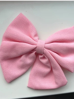 Stor rosa hårrosett med klämma - Söt och trendig hårrosett i ljusrosa tyg med strukturerad yta. Rosetten är stor och har en metallklämma på baksidan som gör den enkel att fästa i håret. Perfekt för att ge din frisyr en extra touch. Materialet är mjukt och formbart.