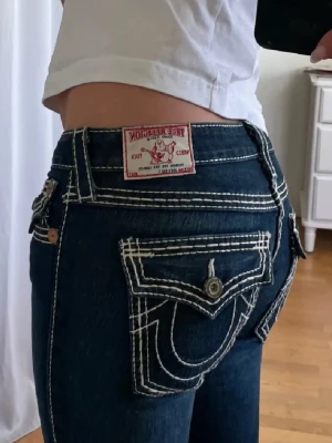 True Religion bootcut jeans mörkblå - Säljer ett par mörkblå bootcut jeans från True Religion med vita kontrastsömmar och stora fickor bak, bilderna är från en tjej jag redan köpt dom av men dom passar tyvärr inte💓