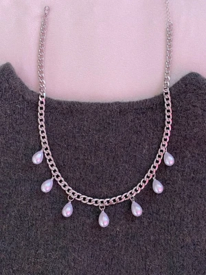 Silverfärgat halsband med pärldroppar - Snyggt halsband i silverfärgad metall med sju droppformade vita pärlor som hänger längs kedjan. Perfekt för att ge en elegant touch till din outfit. Kedjan har en klassisk design och pärlorna ger en trendig vibe.