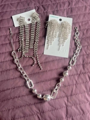 Silvriga statement-örhängen från H&M - Säljer ett par glittrande silvriga statement-örhängen från H&M Conscious. Örhängena har flera rader av små pärlor som hänger i en snygg och vågig form, vilket ger en riktigt cool och trendig look.det är alla tre i ett paket.