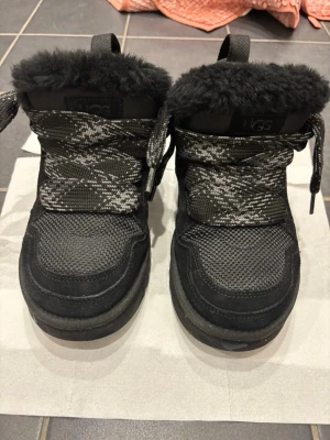 Ugg lowmell herr - Säljer ett par svarta sneakers från UGG med fluffig fuskpäls på insidan och ovankant. Skorna har stickade detaljer och svarta/vita skosnören. Perfekta för dig som vill ha både stil och komfort. Märket syns tydligt på insidan.