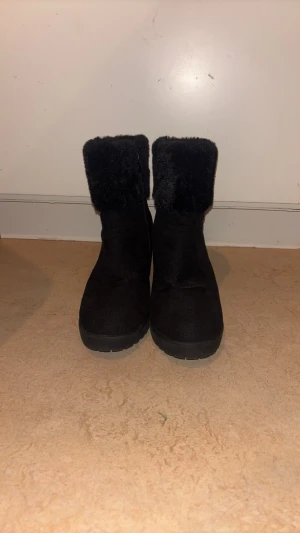 Svarta stövletter med fuskpäls - Säljer ett par svarta stövletter med klack och mjuk fuskpäls runt skaftet. Skorna har en stilren design och grov sula som ger bra grepp. Perfekta för dig som vill ha både värme och stil under kalla dagar. Använt några få antal gånger bara.