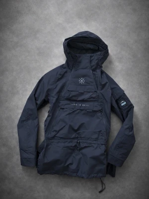 Svart vindjacka från Dope - Snygg svart vindjacka från Dope med stor huva och dragkedja på sidan. Jackan har en stor ficka framtill med diskret logga och patch med bergsmotiv på ärmen. Tillverkad i slitstarkt material, perfekt för blåsiga dagar.