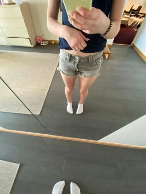 Grå jeansshorts med broderad ficka - Säljer ett par grå jeansshorts med råa kanter och snygg broderad detalj på bakfickan. Shortsen har knappar och fickor både fram och bak. Perfekta för sommaren och ger en avslappnad vibe.