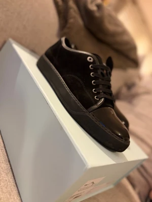 Lanvin - Snygga svarta sneakers med både mocka och lackdetaljer på tån. Skorna har svarta snören, silverfärgade öljetter och en svart sula. Perfekta för dig som gillar en stilren men ändå lite lyxig look storlek 8uk men passar även 42-43.   