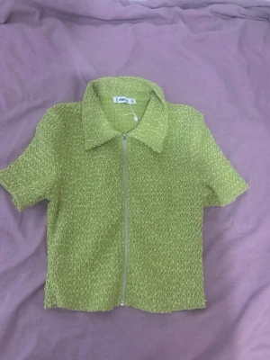 Grön kortärmad topp med dragkedja - Cool grön topp från F21 med korta ärmar och en silverfärgad dragkedja framtill. Materialet är strukturerat och ger en unik känsla. Perfekt för dig som vill sticka ut med en färgglad och trendig look.