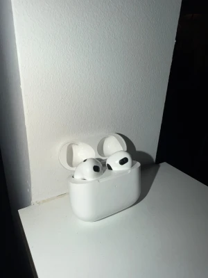 Apple AirPods 3 med laddningsetui - Säljer ett par vita Apple AirPods 3 med trådlöst laddningsetui. Snygg och kompakt design i blank plast, perfekt för dig som vill ha smidiga in-ear hörlurar med grymt ljud och enkel anslutning till iPhone eller andra Apple-enheter.