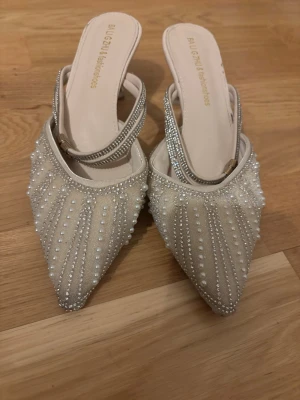 Beige pumps med pärlor från BALGATI - Säljer ett par eleganta beige kitten heels / klackskor från BALGATI med spetsig tå och dekorativa pärlor och strassdetaljer. Skorna har öppen häl och smala remmar med glittrande stenar. Perfekta för dig som vill sticka ut med en lyxig look. Använda fåtal gånger men har små tecken på användning 