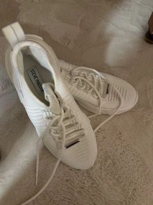 Vita sneakers från Steve Madden - Snygga helvita sneakers från Steve Madden med stickad ovandel och tydliga detaljer i mesh. Skorna har vita snören, grov sula och logga på sidan. Perfekta för dig som gillar en clean och modern look.