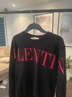 Svart sweatshirt från Valentino - Snygg svart sweatshirt från Valentino med stort rött VALENTINO-tryck över bröstet och ärmarna. Tröjan har rund halsringning och långa ärmar. Perfekt för dig som vill ha en statement-piece i garderoben. Tillverkad i mjukt material för skön känsla.