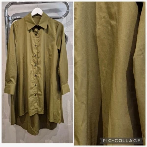 Olivgrön lång skjorta med knappar - Säljer en olivgrön lång skjorta med klassisk krage och knappar framtill. Skjortan har lång ärm och en loose passform som ger en avslappnad look. Perfekt att styla lager på lager eller bära som den är.