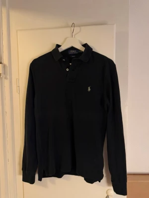 Svart långärmad skjorta från Polo Ralph Lauren - Säljer en svart långärmad skjorta från Polo Ralph Lauren med klassisk krage och knappar framtill. Slim fit-modell med diskret logga broderad på bröstet. Perfekt för dig som gillar stilrena plagg med snygg passform.