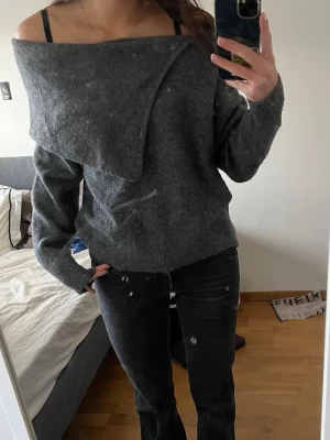 Mörkgrå off shoulder stickad tröja - Snygg mörkgrå stickad tröja med off shoulder-design och bred krage som viks ner över axlarna. Tröjan har lång ärm och är gjord i mjukt material