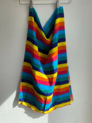 Tygbit med silkeskänsla  - Färgglatt tygstycke med breda horisontella ränder i blått, gult, rött, orange och grönt. Tygbiten har en mjuk och följsam känsla och kan användas till DIY-projekt, dekoration eller som accessoar. Materialet ser ut att ha silkeskänsla.