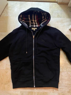 Burberry kofta - Säljer min burberry kofta som jag har tagit på mig några gånger. Den har inga tecken på användning förutom metallbiten som saknas på snöret. Som ni ser på bilden. Den är i large men känns som medium.  Pris går att diskuteras 