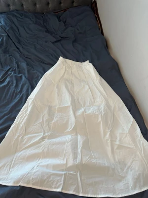 Vit långkjol med resårmidja - Snygg vit långkjol med enkel och luftig design. Kjolen har resår i midjan för en bekväm passform och är tillverkad i ett lätt tyg som passar perfekt till varmare dagar. Stilren och enkel att matcha med olika toppar.