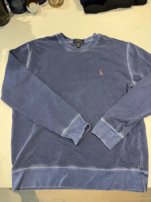 Blå sweatshirt från Polo Ralph Lauren - Säljer en blå sweatshirt från Polo Ralph Lauren med rund halsringning och långa ärmar. Tröjan har vita kontrastsömmar och den klassiska röda logotypen broderad på bröstet. Storlek 18-20 men samma sak som xs men fungerar även som S